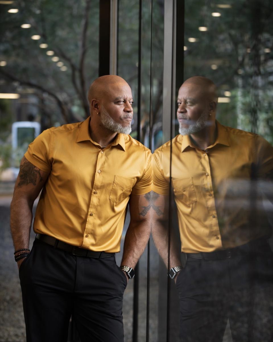 Princeton Clark in a gold shirt reflected in glass